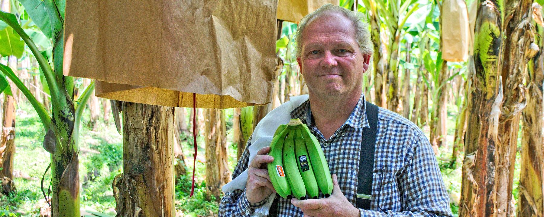 Der Bananenproduzent Louis Hesselholt hält stolz seine Ernte in den Händen. Er steht in seiner Plantage.