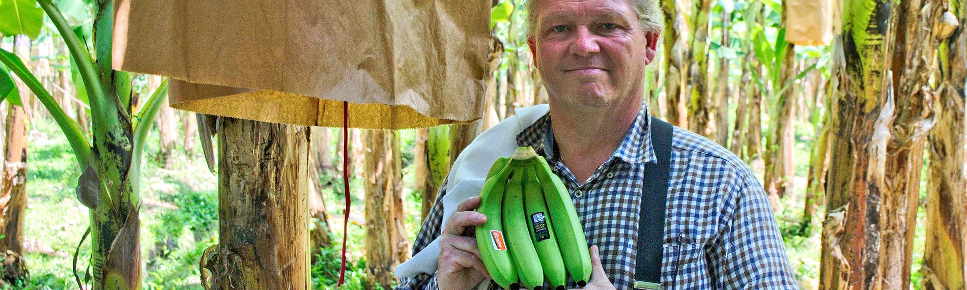 Der Bananenproduzent Louis Hesselholt hält stolz seine Ernte in den Händen. Er steht in seiner Plantage.