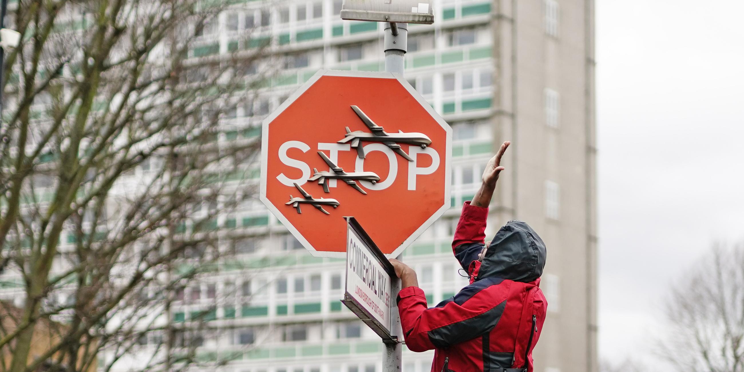 Großbritannien, London: Ein Mann entfernen ein Stoppschild auf dem drei Drohnen gemalt sind. 