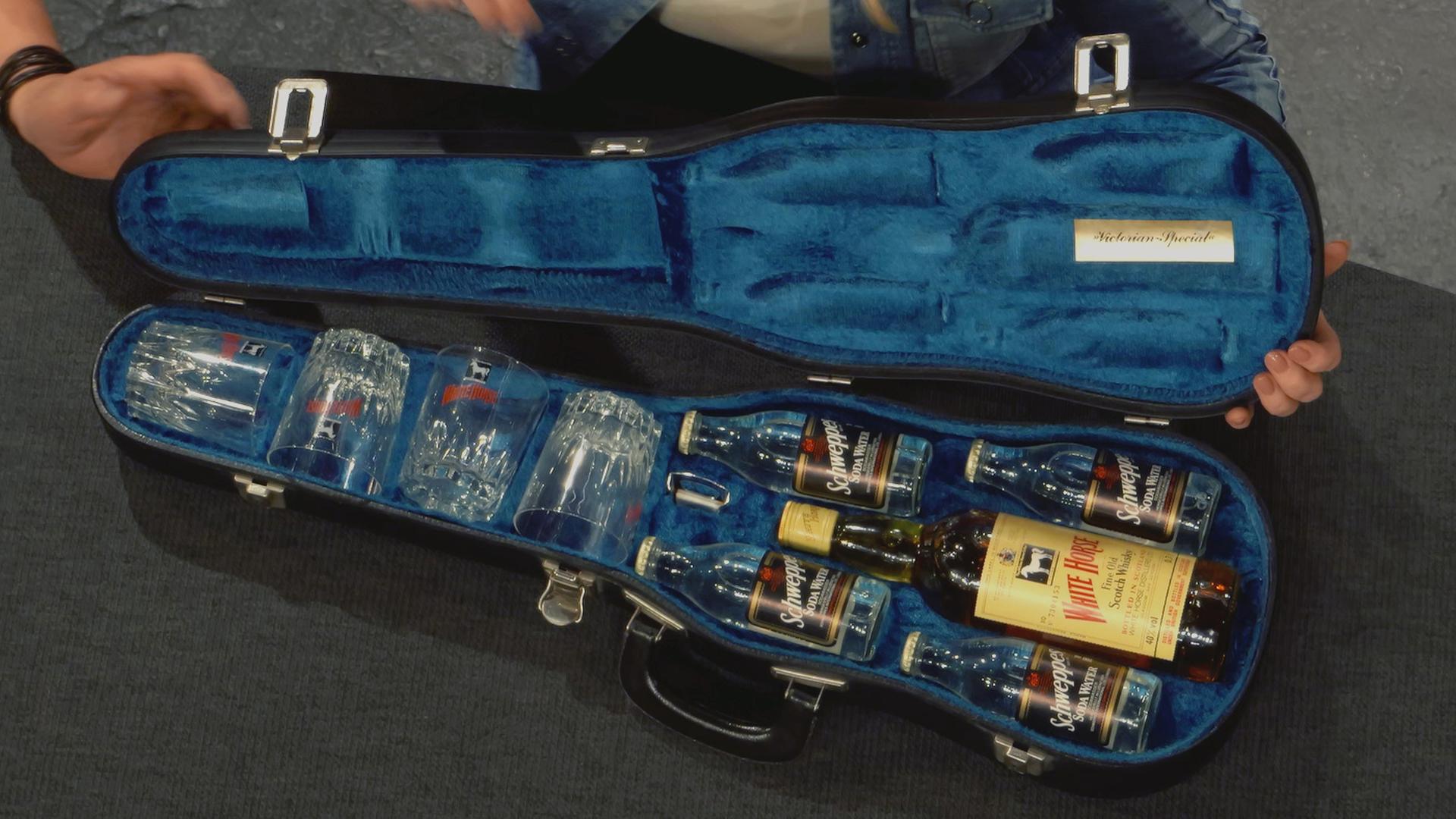 Alter Geigenkoffer mit blauem Futter. Innen befinden sich vier Whiskey-Gläser, eine White-Horse Whiskey-Flasche und 4 kleinere Schweppes-Flaschen.