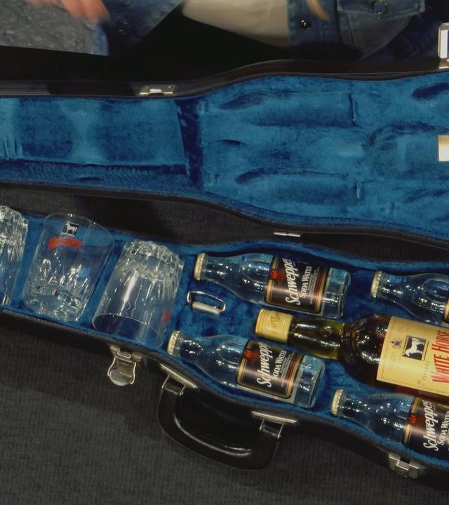 Alter Geigenkoffer mit blauem Futter. Innen befinden sich vier Whiskey-Gläser, eine White-Horse Whiskey-Flasche und 4 kleinere Schweppes-Flaschen.