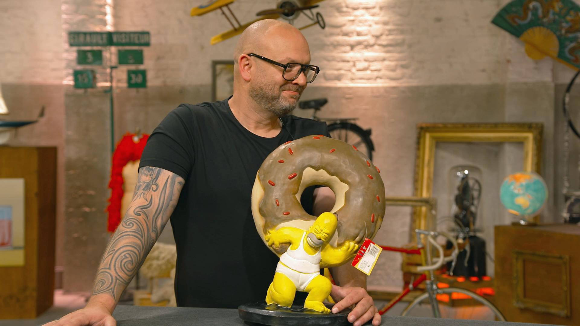 Sven Deutschmanek steht grinsend hinter einer Latex-Figur von Homer Simpson. Dieser stemmt einen übergroßen Donut.