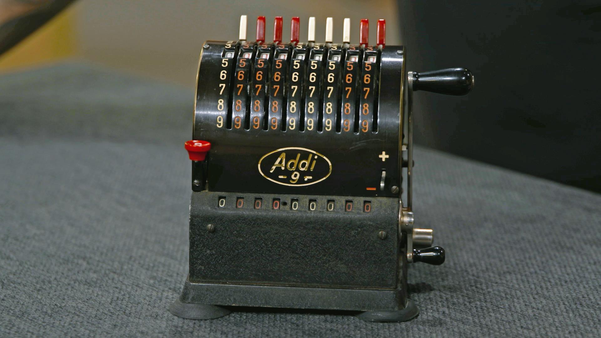 Kleine, antike Rechenmaschine in schwarz mit rot-weißen Ziffern.