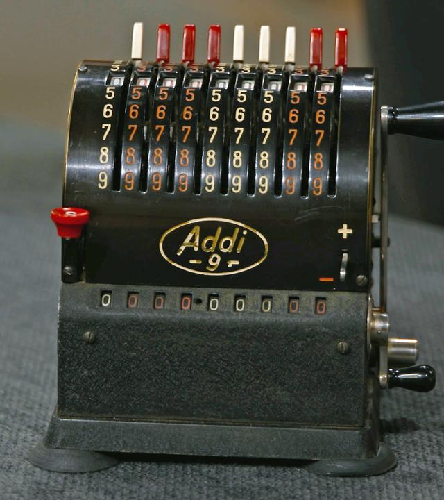 Kleine, antike Rechenmaschine in schwarz mit rot-weißen Ziffern.