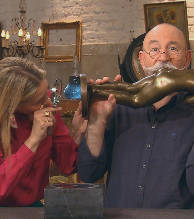 Horst Lichter hält eine Bronzestatuette, die Expertin Dr. Bianca Berding mit einer Lupe begutachtet