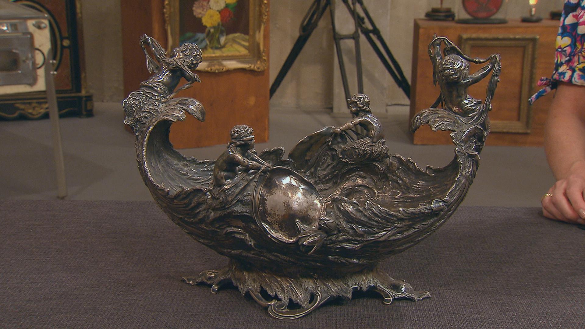 Eine silberne Schale, Jardinière genannt, in die Wellenformen und Meermenschen eingearbeitet sind.