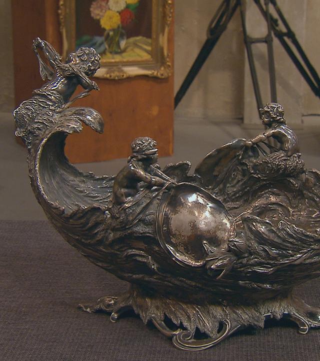 Eine silberne Schale, Jardinière genannt, in die Wellenformen und Meermenschen eingearbeitet sind.