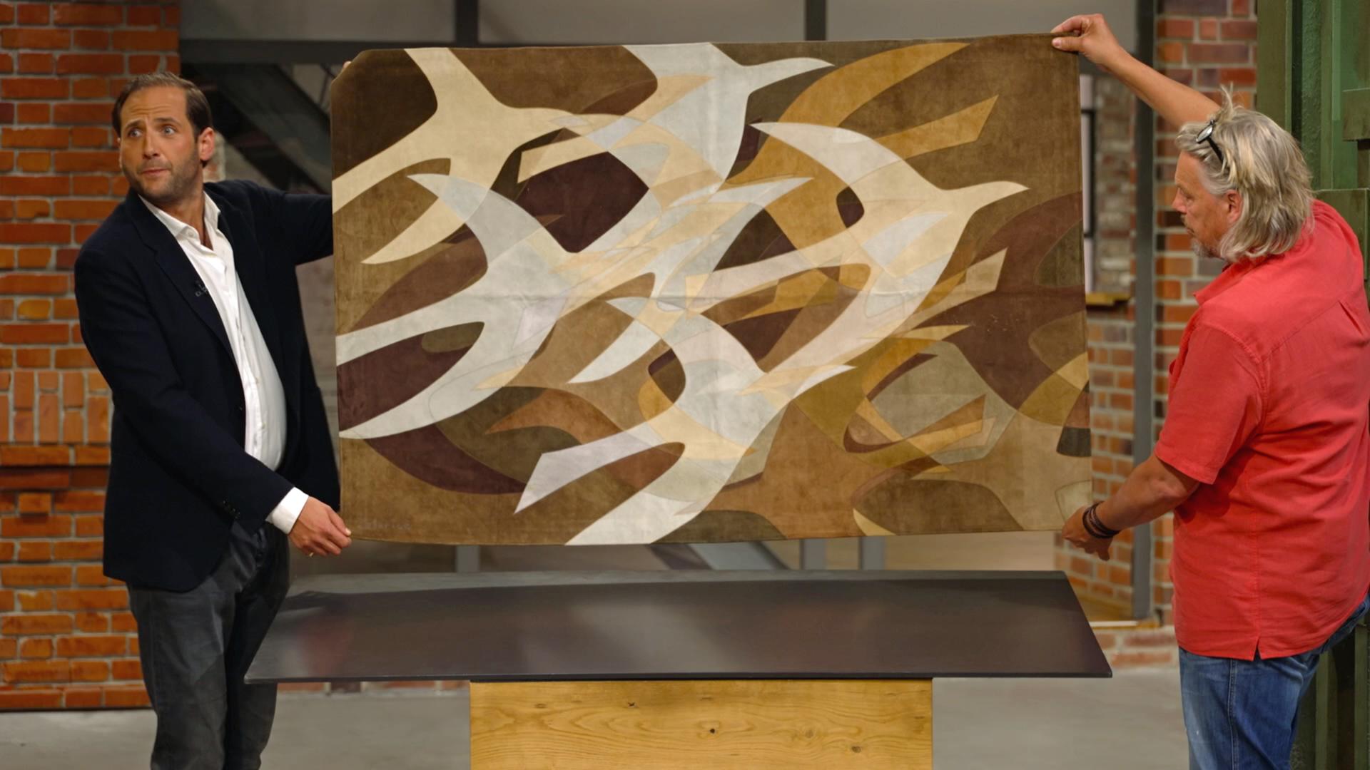 Julian Schmitz-Avila und Jos van Katwijk halten einen Wandteppich mit Vogel-Motiv hoch.