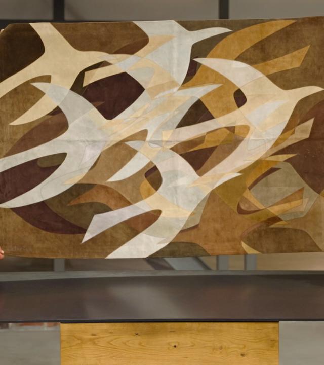 Julian Schmitz-Avila und Jos van Katwijk halten einen Wandteppich mit Vogel-Motiv hoch.