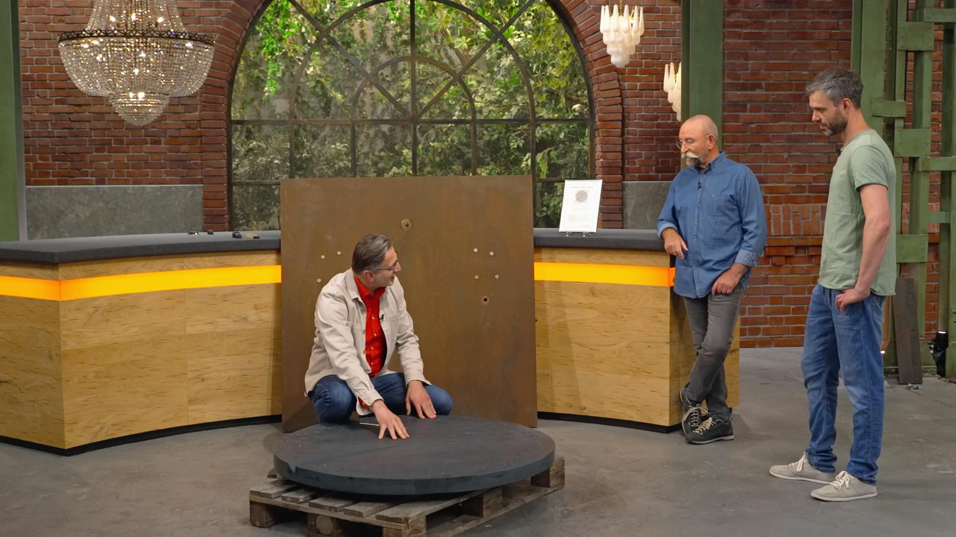 Detlev Kümmel, Horst Lichter und ein Verkäufer begutachten eine große, runde Schieferplatte im Händlerraum. 