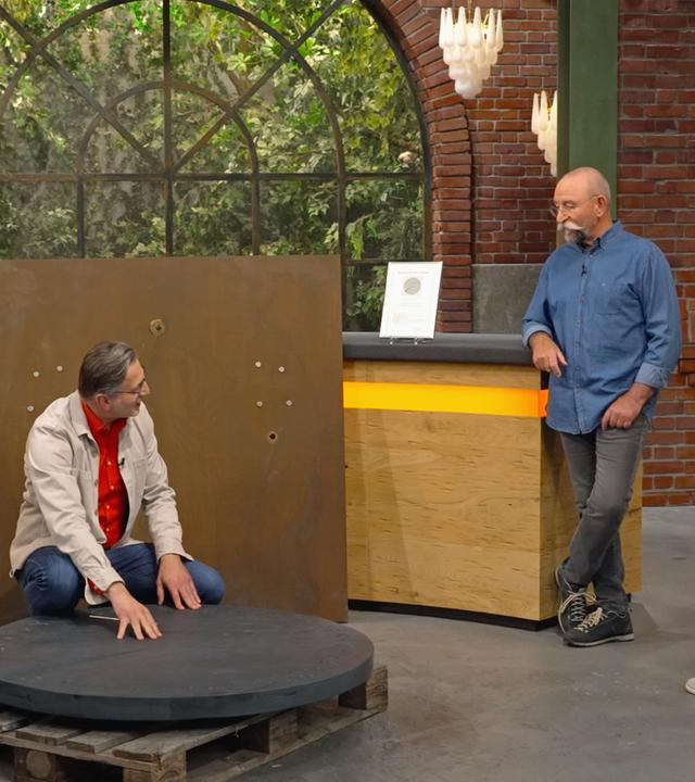 Detlev Kümmel, Horst Lichter und ein Verkäufer begutachten eine große, runde Schieferplatte im Händlerraum. 