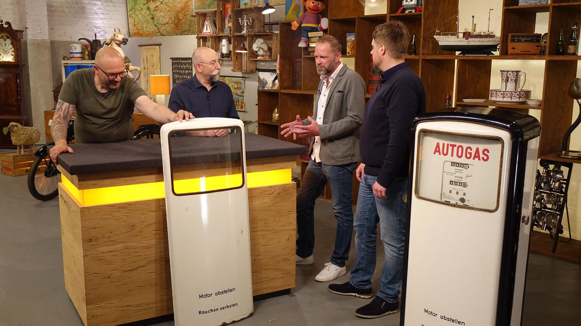Sven Deutschmanek begutachtet eine Zapfsäule. Horst Lichter und zwei Verkäufer stehen mit dem Experten am Expertisentisch.