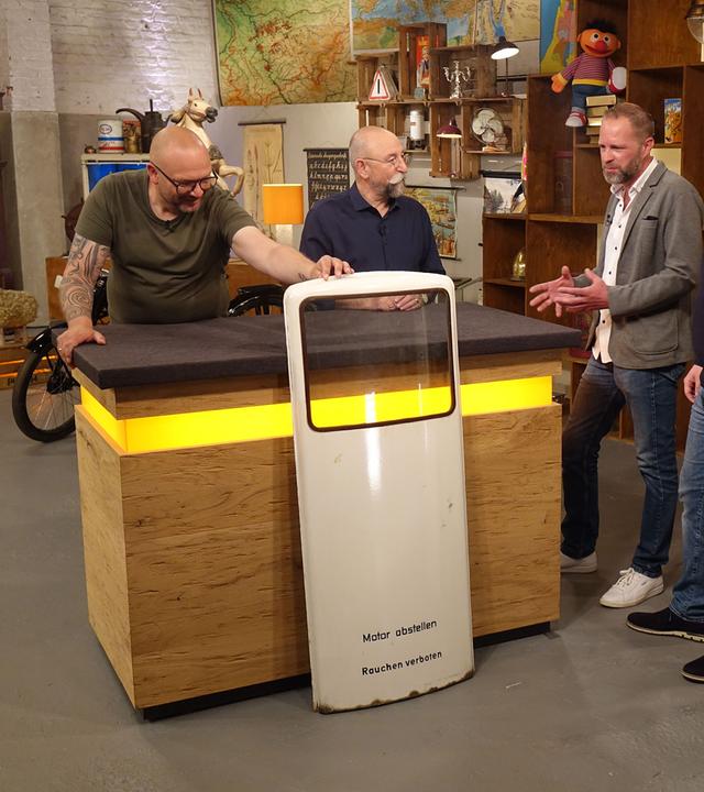 Sven Deutschmanek begutachtet eine Zapfsäule. Horst Lichter und zwei Verkäufer stehen mit dem Experten am Expertisentisch.