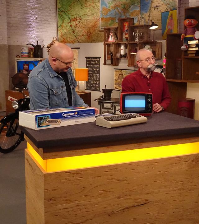 Experte Sven Deutschmanek begutachtet einen "C64" von Commodore. Neben ihm am Expertentisch stehen Horst Lichter, die Verkäuferin und der Verkäufer.