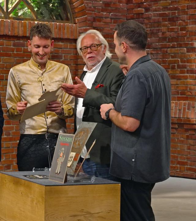 Die Händlerrunde steht um ein Konvolut alter Werbeschilder herum und begutachtet diese genauer.