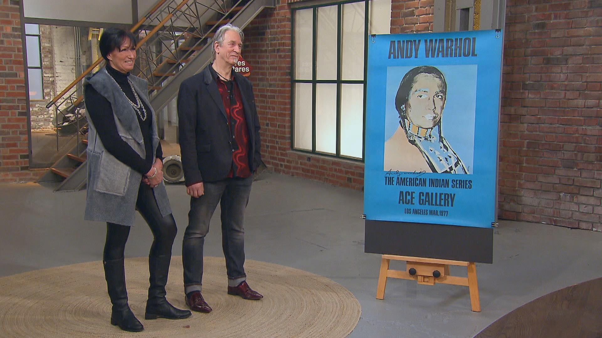 Neben einem Poster von Andy Warhol stehen die Verkäuferin und der Verkäufer des Plakats im Händlerraum.