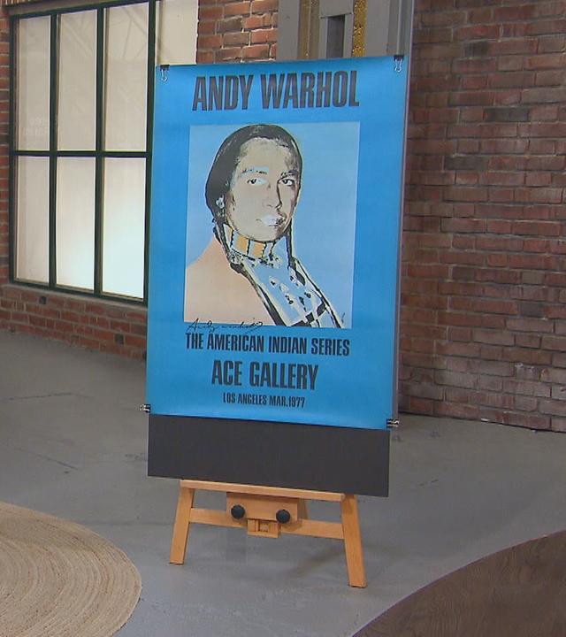 Neben einem Poster von Andy Warhol stehen die Verkäuferin und der Verkäufer des Plakats im Händlerraum.