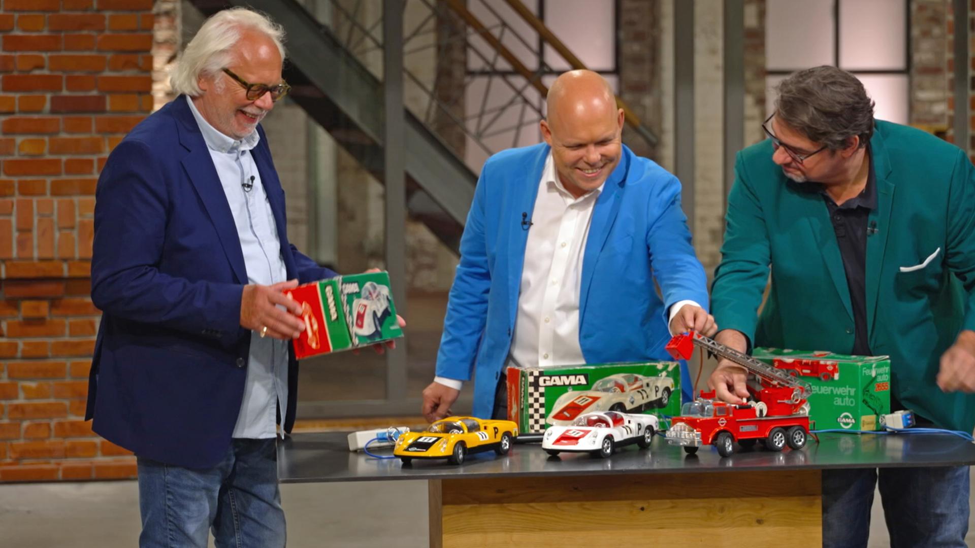 Die Herren der Händlerrunde spielen mit einem Konvolut von Spielzeug-Autos.