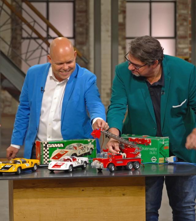 Die Herren der Händlerrunde spielen mit einem Konvolut von Spielzeug-Autos.