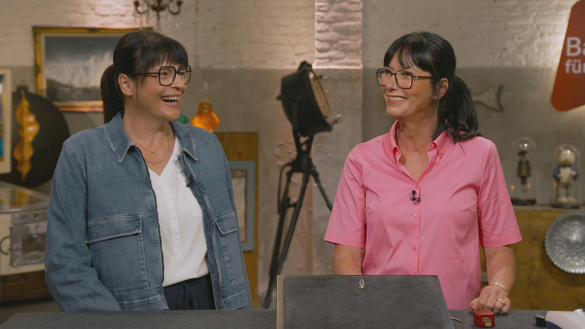 Heide Rezepa-Zabel und eine Verkäuferin stehen nebeneinander und strahlen sich an. Sie sehen sich sehr ähnlich. 