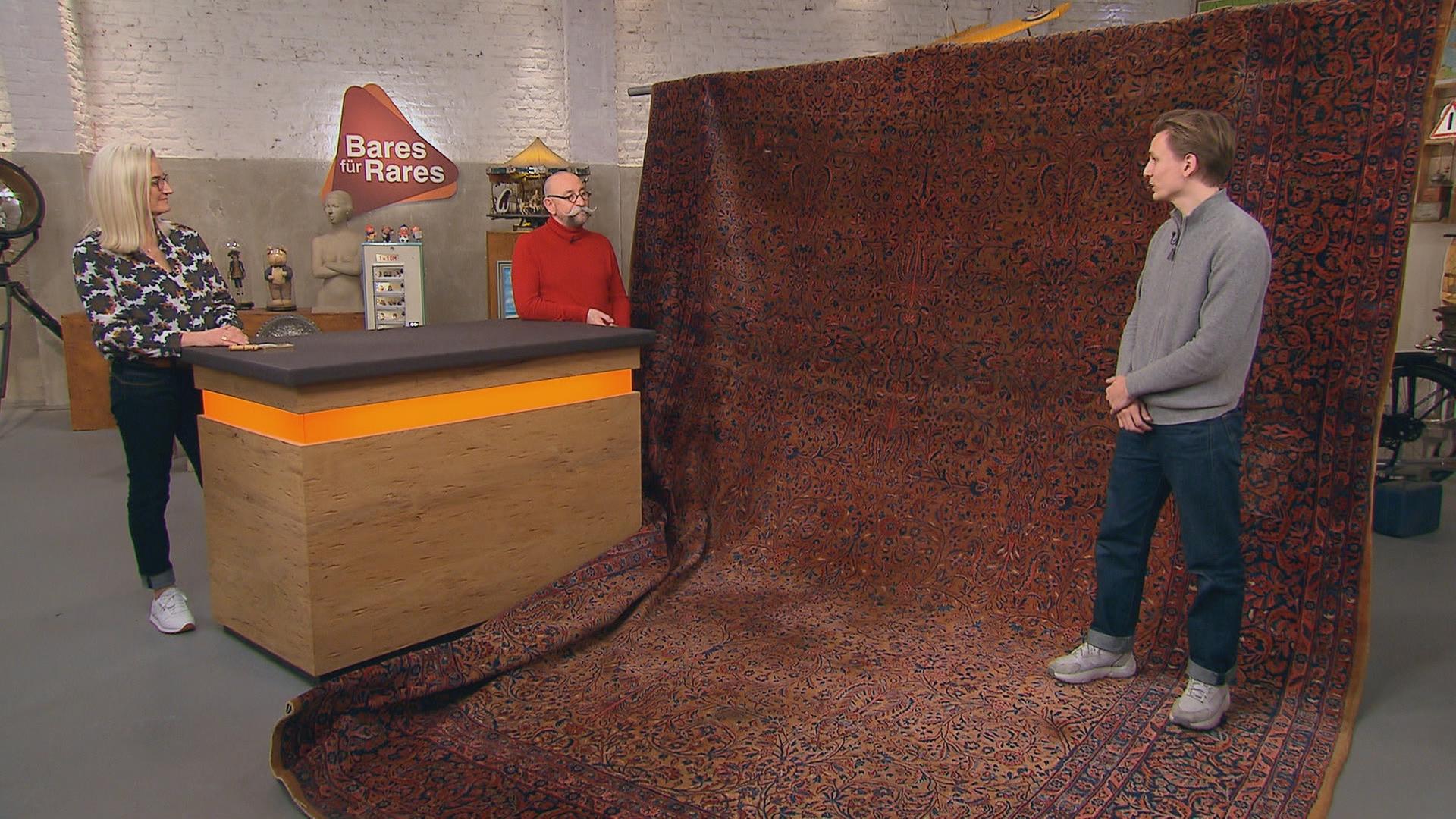 Expertin Dr. Friederike Werner begutachtet einen knapp 25 Quadratmeter großen Keshan-Teppich. Neben ihr stehen Horst Lichter und der Verkäufer des Teppichs.