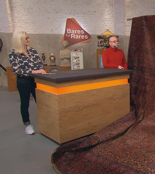 Expertin Dr. Friederike Werner begutachtet einen knapp 25 Quadratmeter großen Keshan-Teppich. Neben ihr stehen Horst Lichter und der Verkäufer des Teppichs.