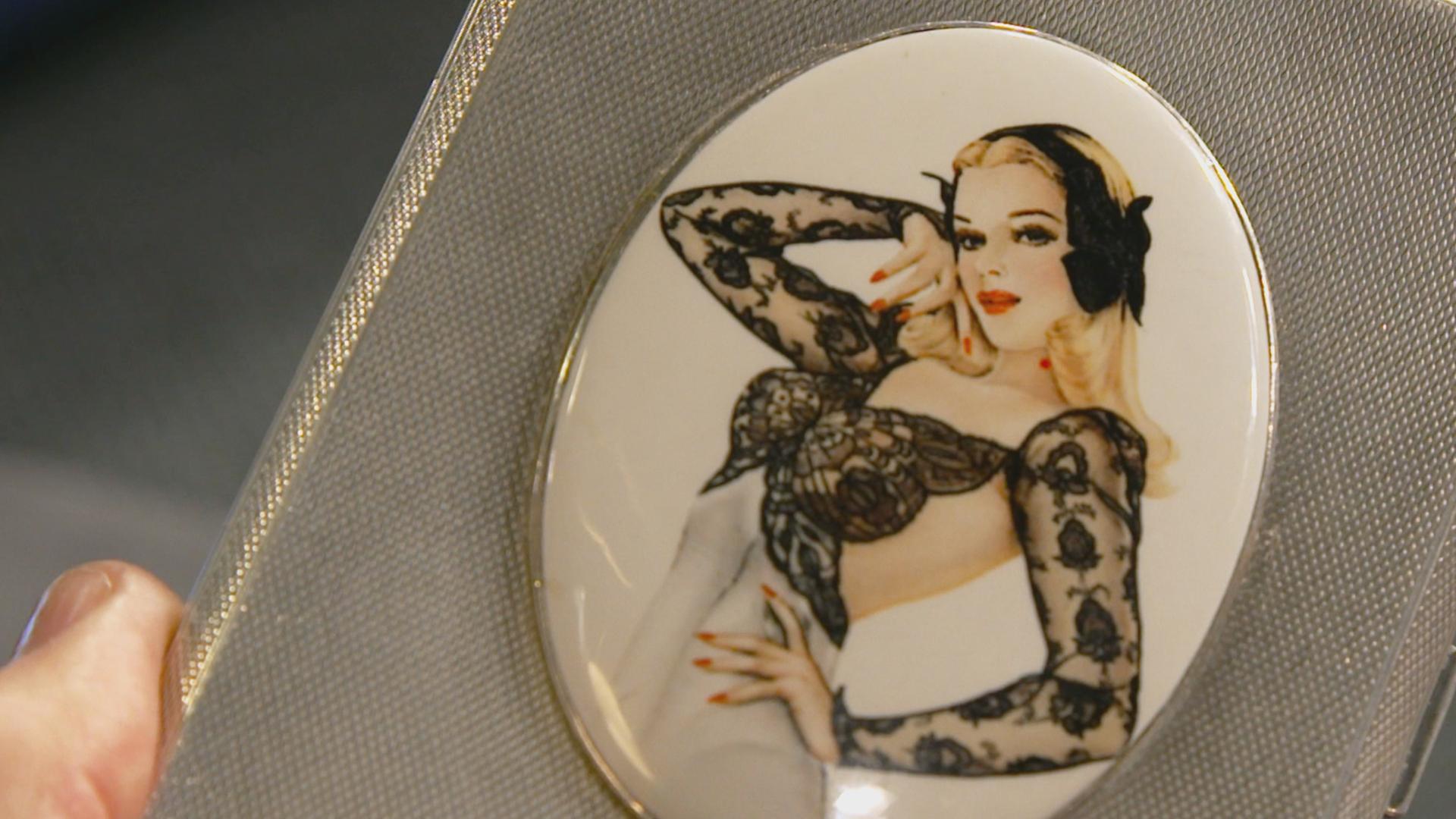 Ein silbernes Zigaretten-Etui mit einem blonden Pin-up-Girl.