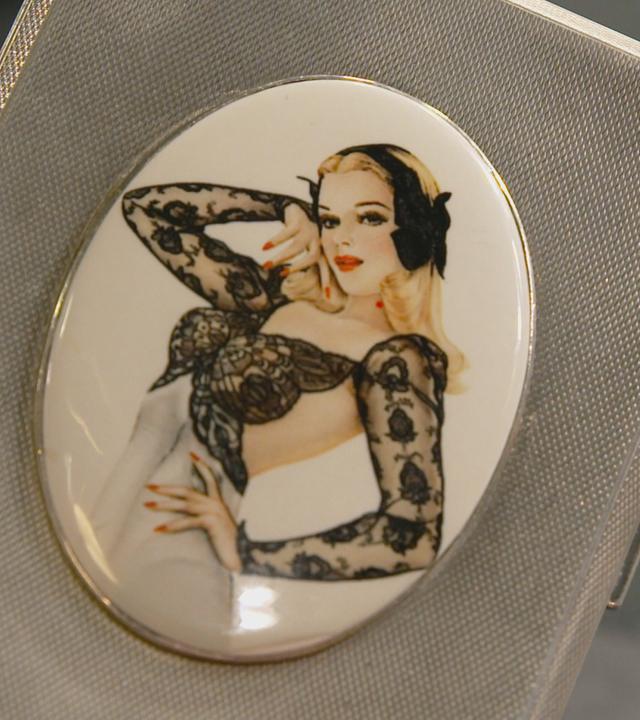 Ein silbernes Zigaretten-Etui mit einem blonden Pin-up-Girl.