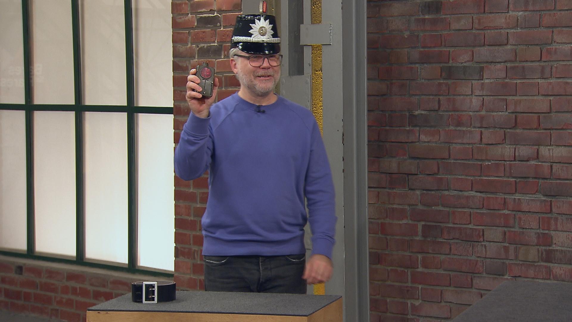 Einer der Händler hat sich eine historische Polizeimütze aufgesetzt und hält ein altes Kontrollgerät in der Hand.