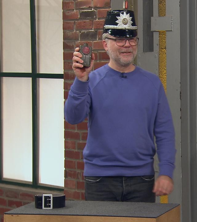 Einer der Händler hat sich eine historische Polizeimütze aufgesetzt und hält ein altes Kontrollgerät in der Hand.