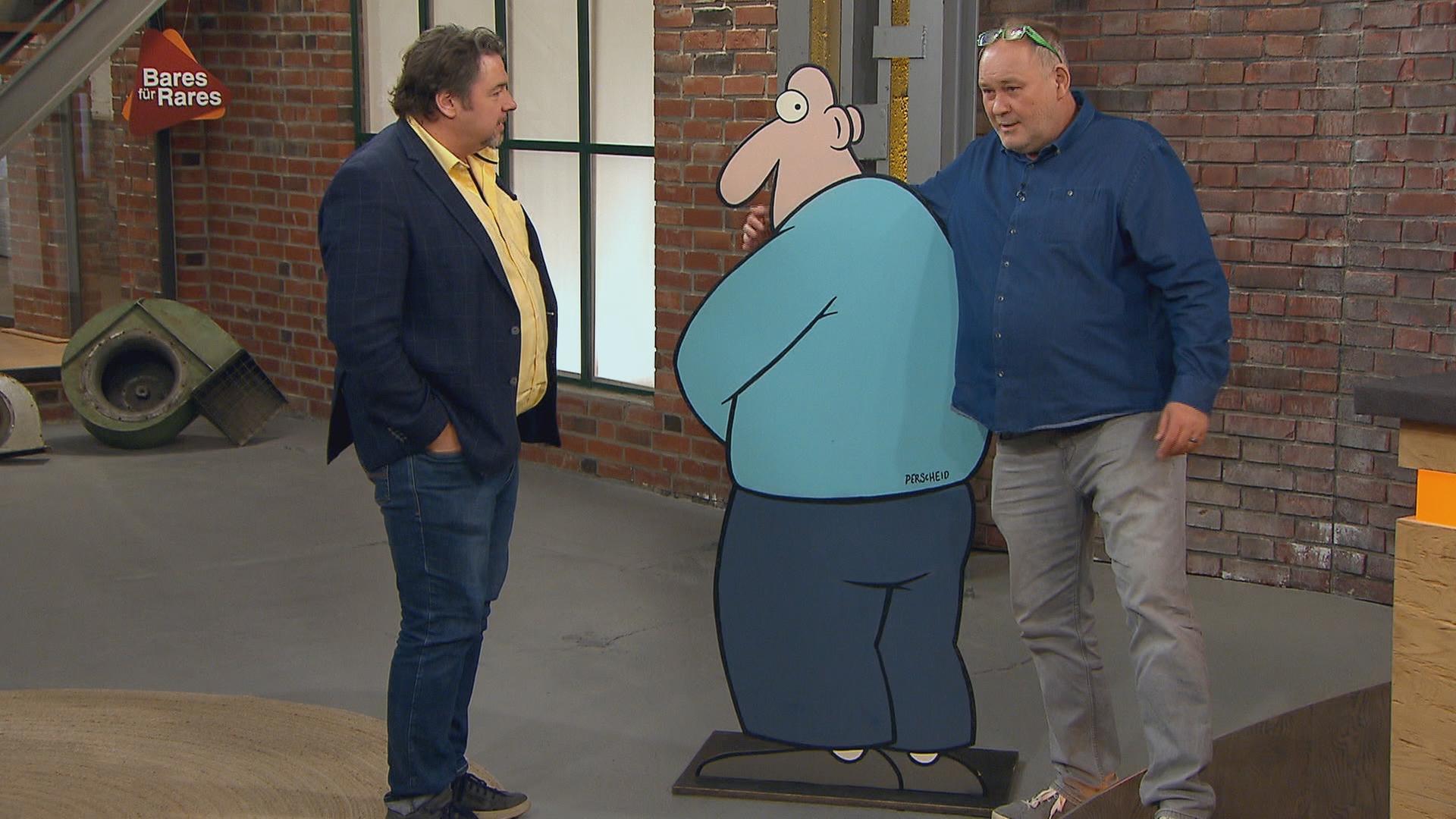 Die Händler Daniel Meyer und Walter "Waldi" Lehnertz stehen neben einem Pappaufsteller des Cartoonisten Martin Perscheid