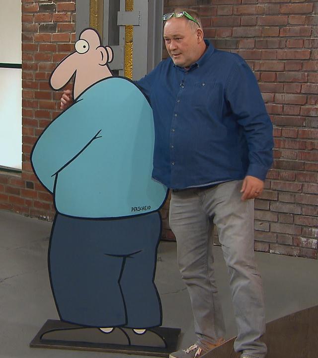 Die Händler Daniel Meyer und Walter "Waldi" Lehnertz stehen neben einem Pappaufsteller des Cartoonisten Martin Perscheid