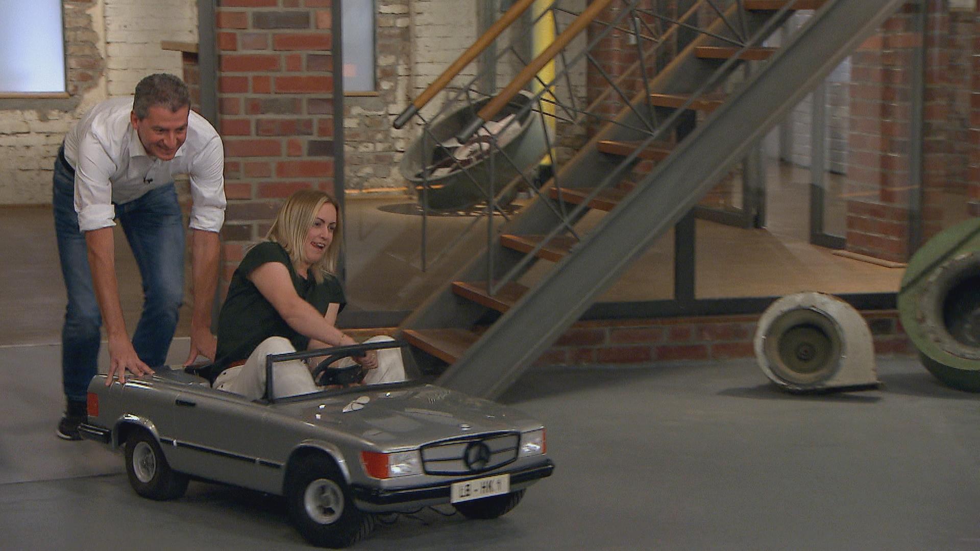 Der Verkäufer eines Mercedes SL 500 Mini schiebt das Auto in den Händlerraum. Hinterm Steuer des Wagens sitzt die Verkäuferin.