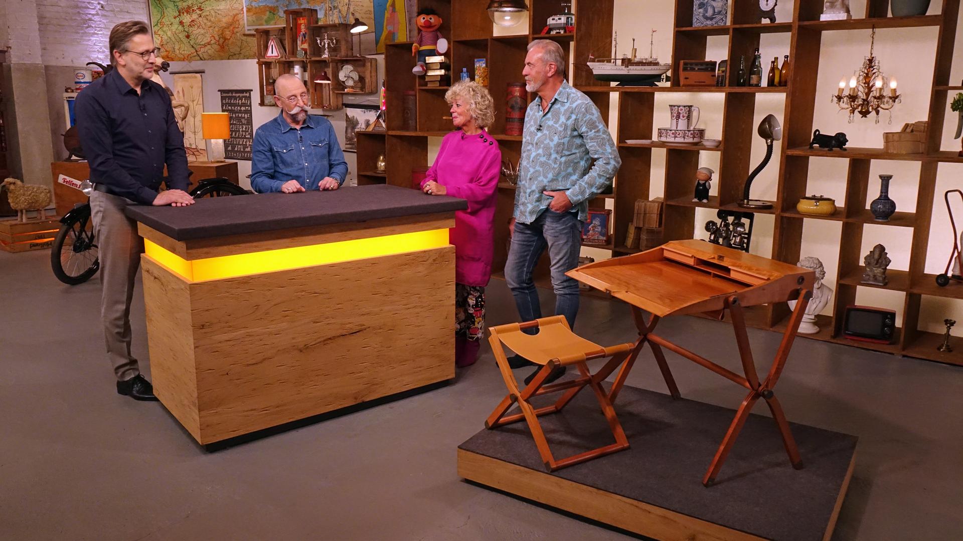 Horst Lichter, Experte Detlev Kümmel und ein Verkäuferpaar im Expertisenraum. Daneben ein Schreibpult mit Hocker von Hermès.