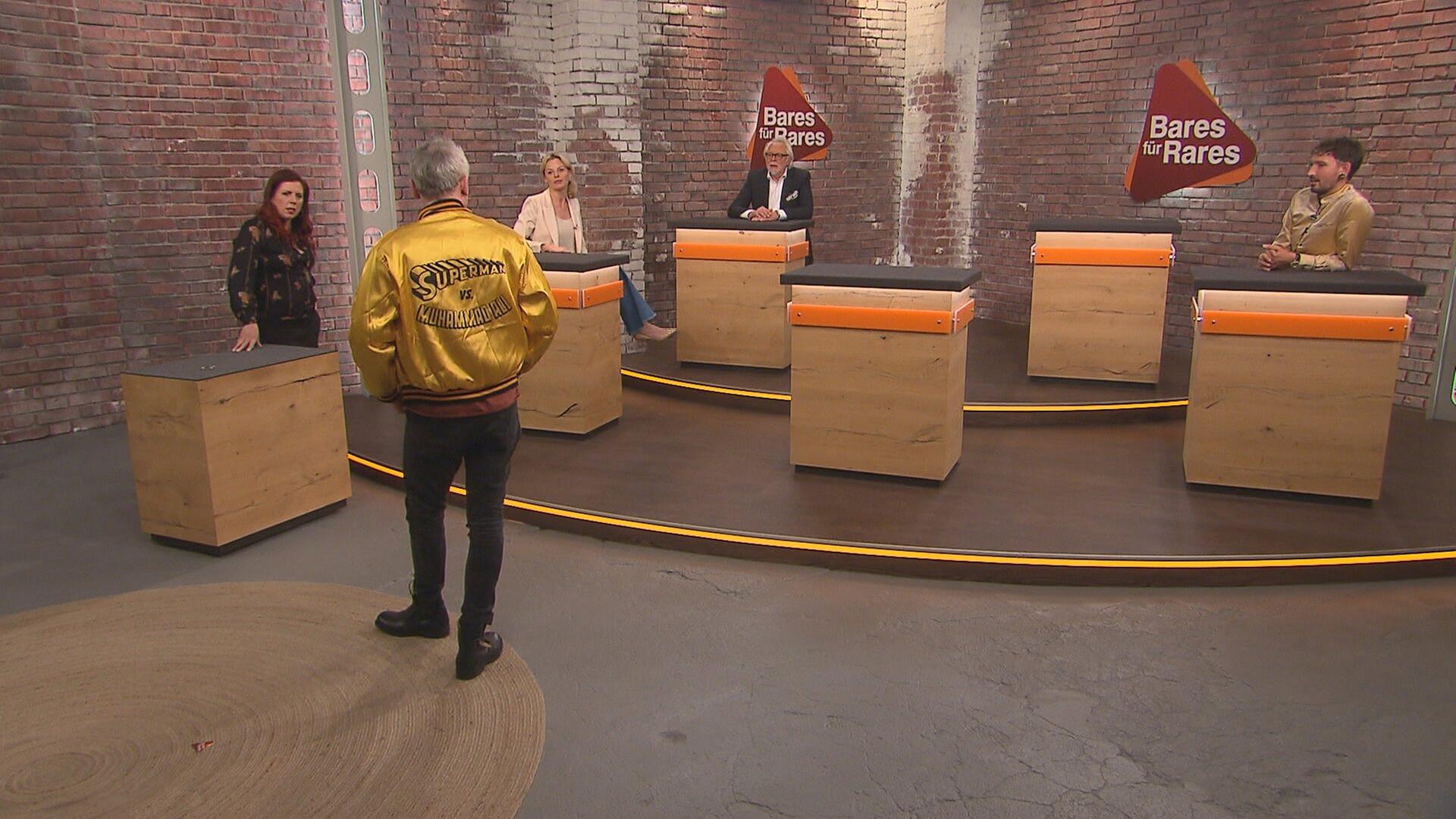 Händler Christian Vechtel posiert im Händlerraum in einer Jacke von Angelo Dundee auf der "Superman vs. Muhammad Ali" aufgedruckt ist