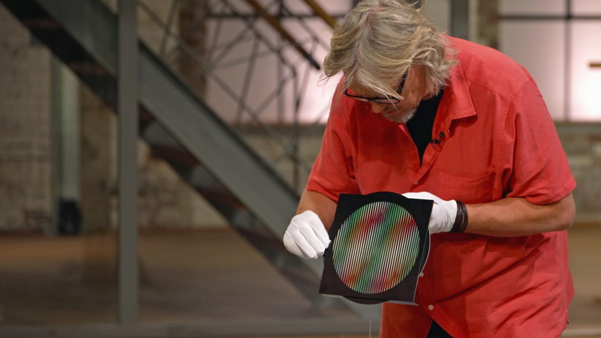 Jos van Katwijk begutachtet einen Siebdruck auf Plexiglasscheibe aus der Nähe.