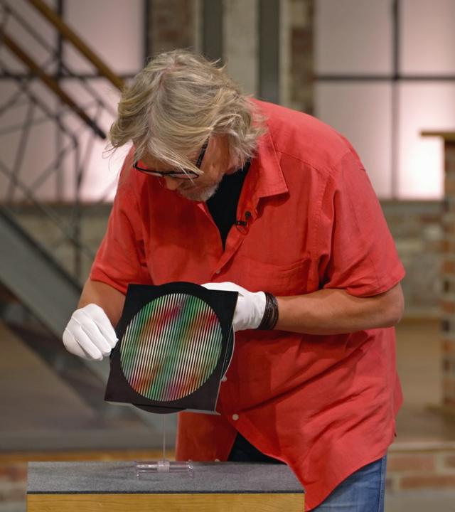 Jos van Katwijk begutachtet einen Siebdruck auf Plexiglasscheibe aus der Nähe.