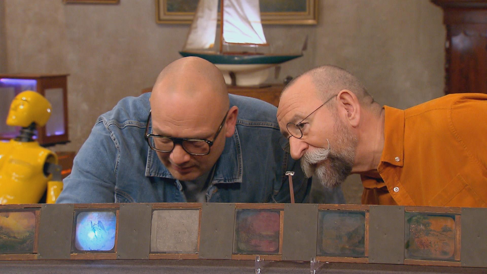 Experte Sven Deutschmanek und Horst Lichter beugen sich über eine Holzlatte mit Glasbildern.