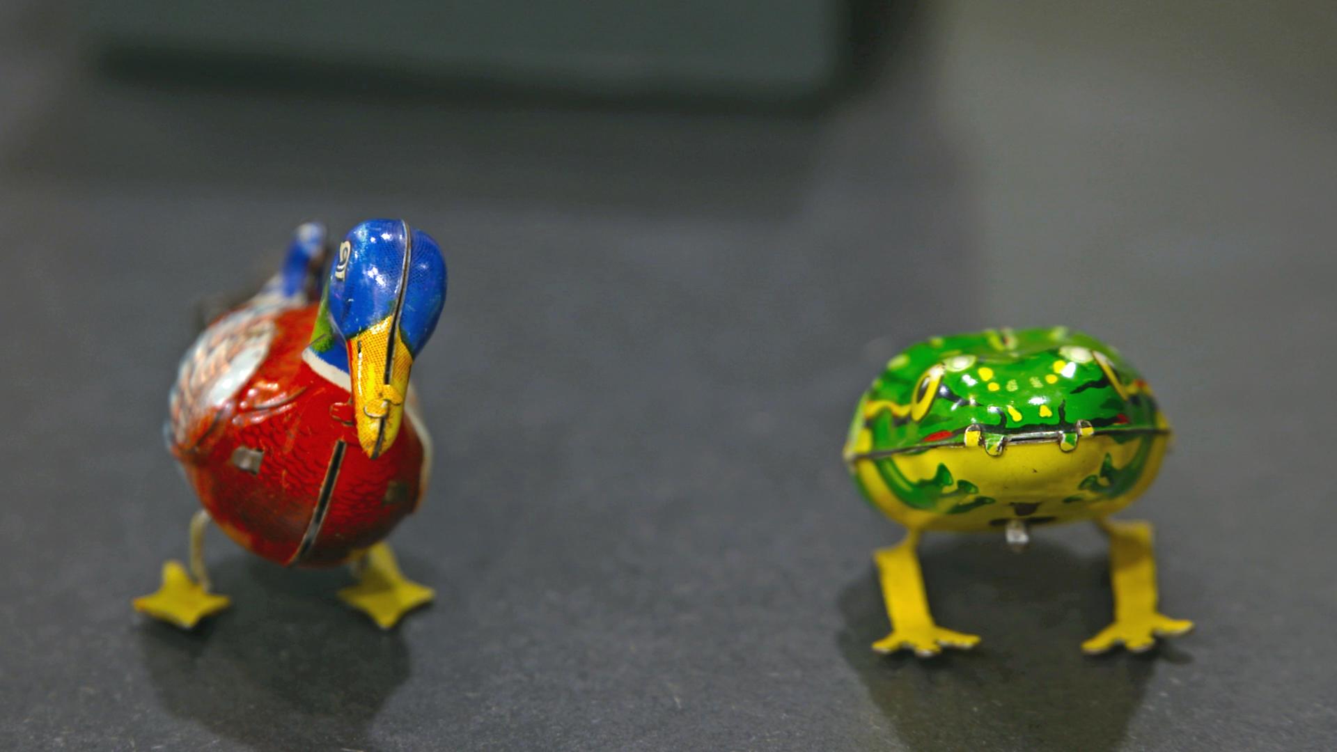 Zwei Blechspielzeugfiguren: Eine Wackel-Ente und ein Hüpf-Frosch