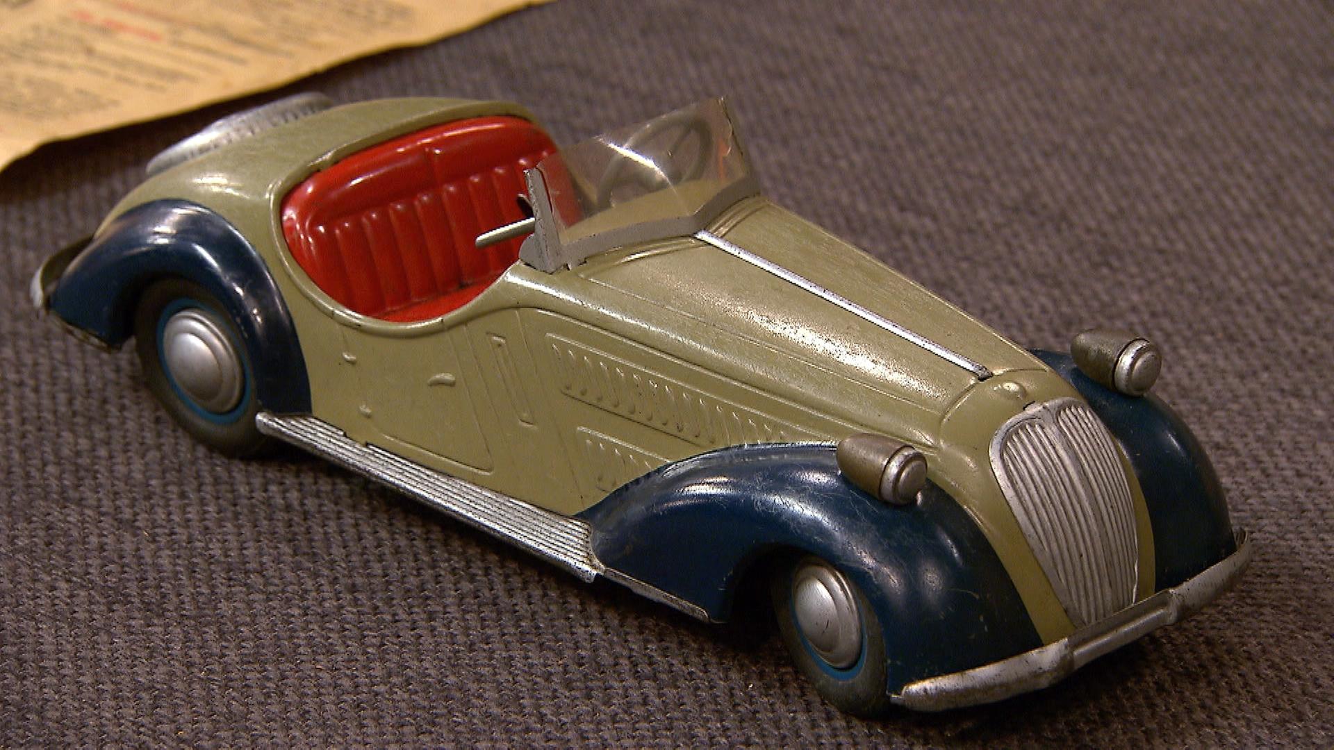 Ein altes Spielzeugauto im Stil eines Oldtimers liegt auf dem Expertisentisch.