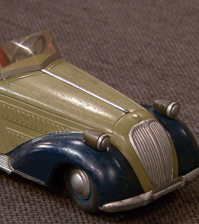 Ein altes Spielzeugauto im Stil eines Oldtimers liegt auf dem Expertisentisch.