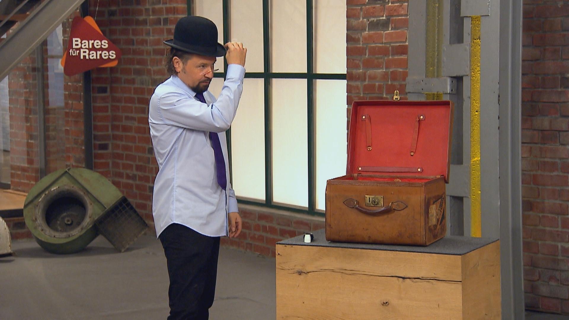 Einer der Händler steht neben einem altmodischen Koffer und setzte sich einen Filzhut, auch Melone genannt, auf.