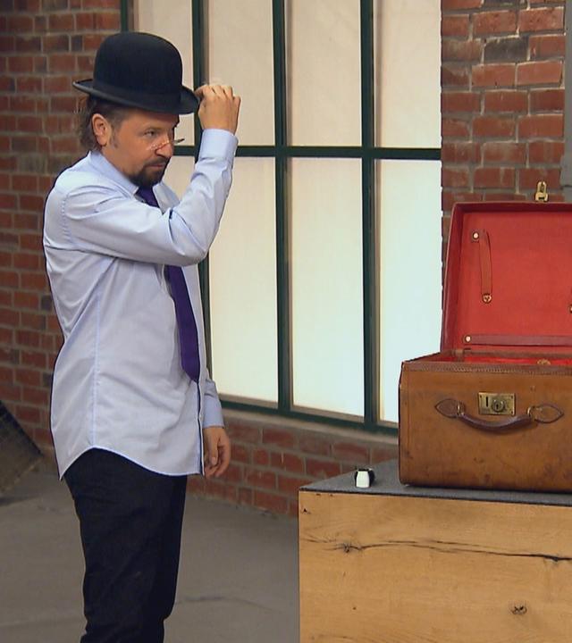 Einer der Händler steht neben einem altmodischen Koffer und setzte sich einen Filzhut, auch Melone genannt, auf.