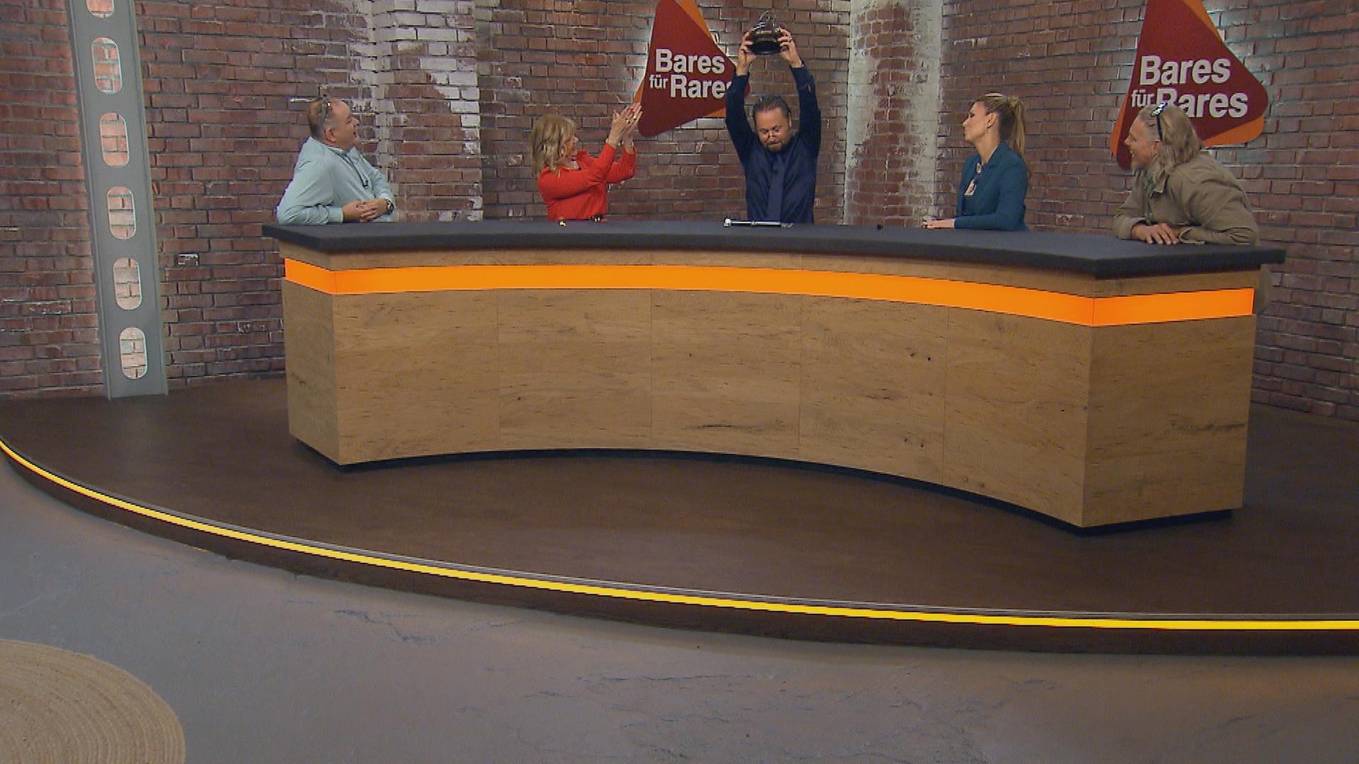 Walter „Waldi“ Lehnertz, Elke Velten, Wolfgang Pauritsch, Sarah Schreiber und Jos van Katwijk sitzen am Händlerpult. Wolfgang Pauritsch hält eine Kupferdose in die Luft.