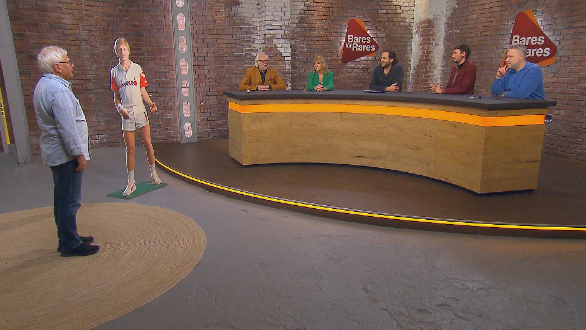 Im Händlerraum steht ein Werbeaufsteller von Boris Becker und daneben der Verkäufer des Aufstellers. Davor sitzt das fünfköpfige Händlerteam.