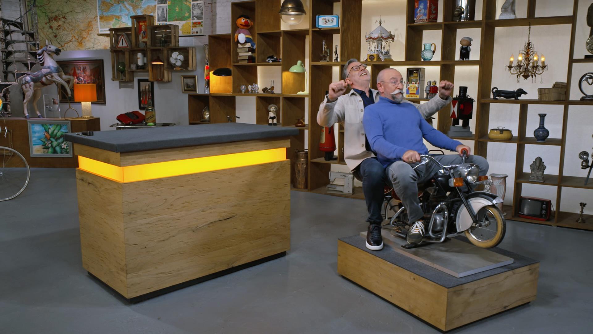 Detlev Kümmler und Horst Lichter sitzen auf einem alten Kinderkarusell-Motorrad.