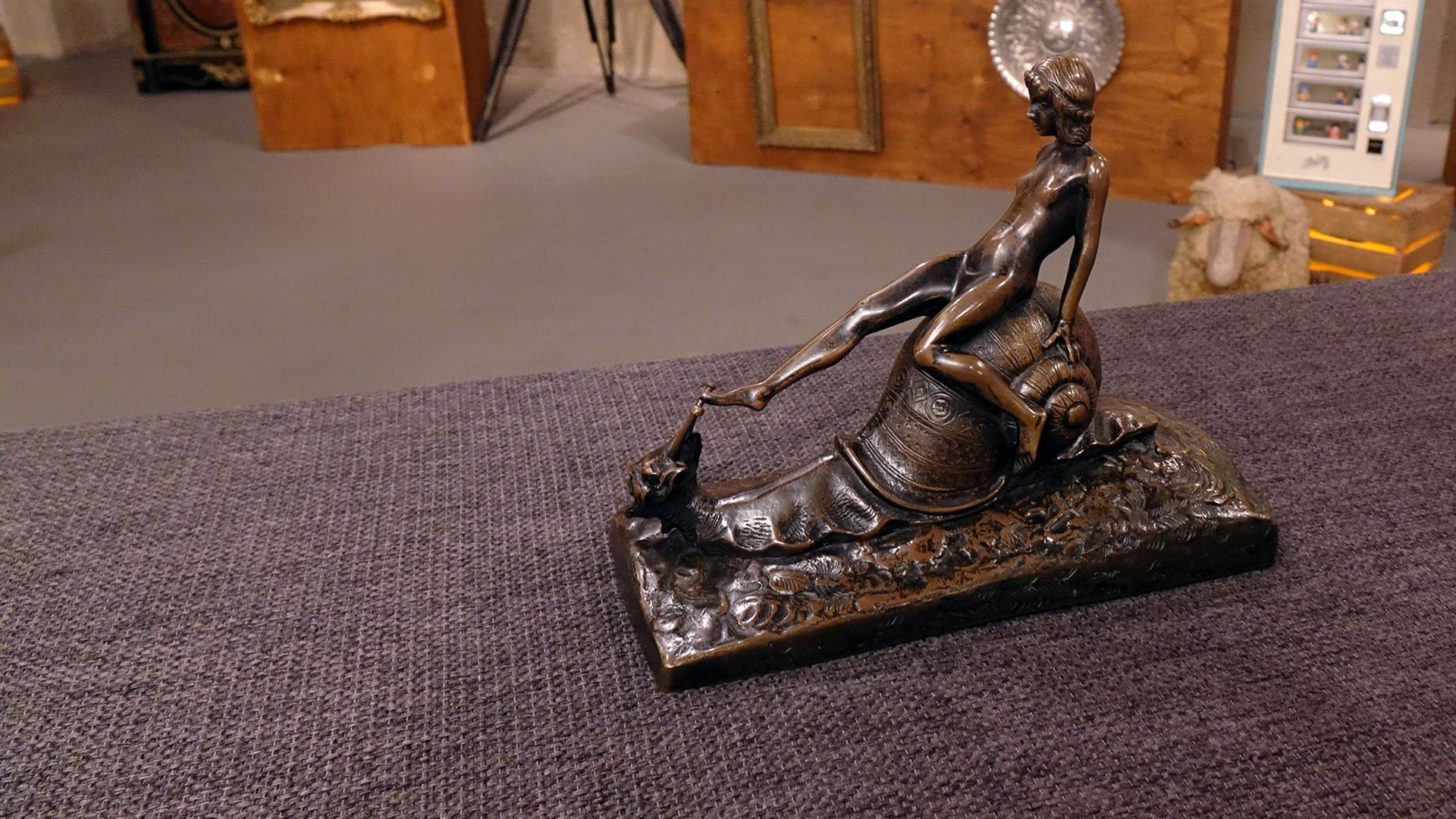 Bronzefigur einer nackten Frau, die auf einer Schnecke sitzt.