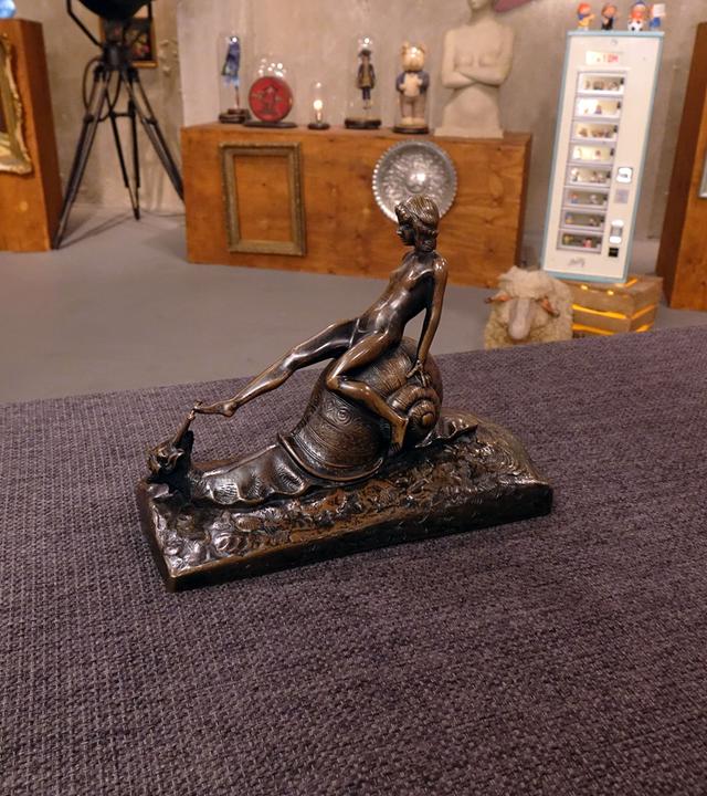 Bronzefigur einer nackten Frau, die auf einer Schnecke sitzt.
