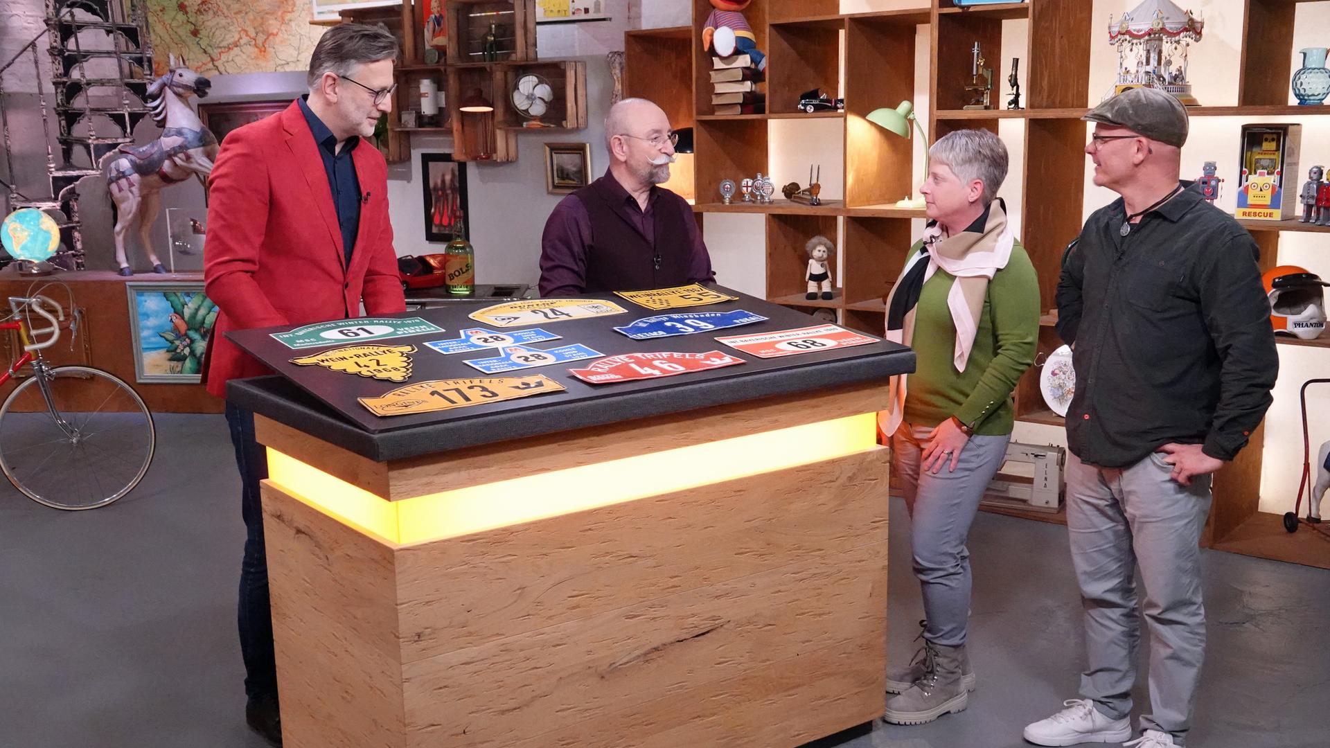 Detlev Kümmel und Horst Lichter begutachten mit den beiden Verkäufern Judith Nicoleit und Thorsten Fuchs eine Sammlung alter Rallye-Schilder aus dem Motorsport.