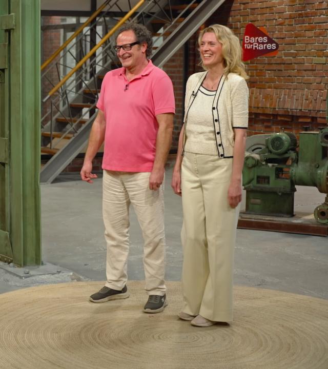 Im Händlerraum steht rechts ein Verkäuferpaar und strahlt. Links steht das Objekt: Ein überdimensionaler, brauner Lederstiefel.